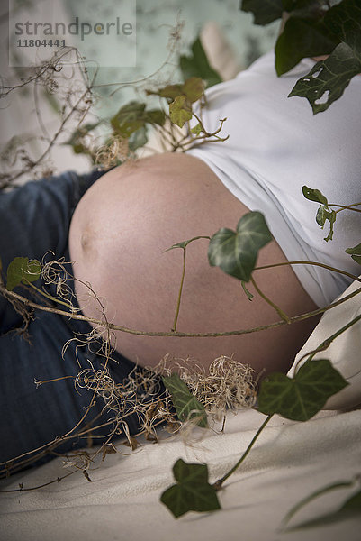 Midsection der schwangeren Frau mit Zweig der grünen Efeublätter gewickelt