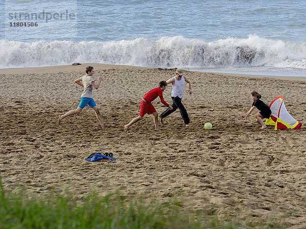 Mädchen und Jungen spielen Fußball mit Vater am Strand