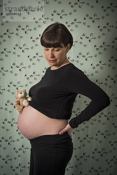 Schwangere Frau hält Teddybär auf ihrem Bauch