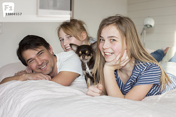 Vater mit Töchtern und Hund auf dem Bett