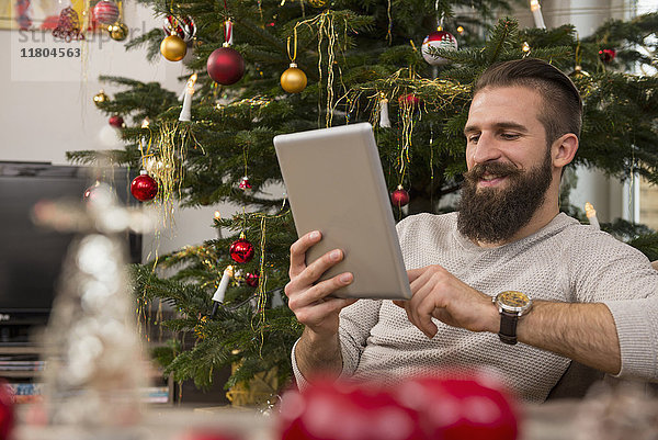 Junger Mann mit digitalem Tablet gegen Weihnachtsbaum