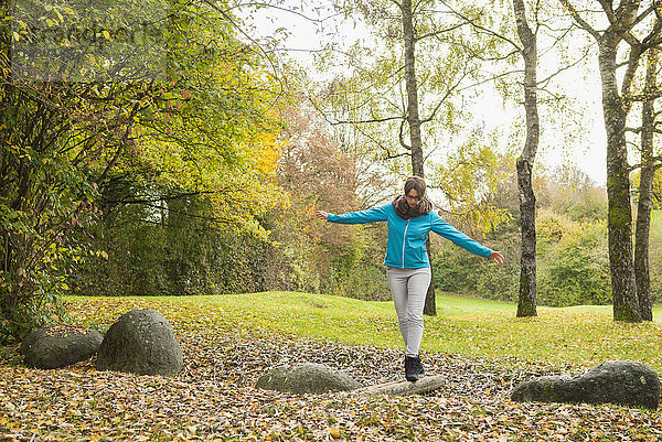 Frau balanciert auf Baumstamm in Herbstlandschaft im Hintergrund
