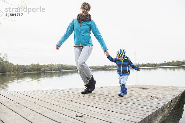 Lächelnde Mutter mit Sohn  der auf einem Holzsteg über den See läuft