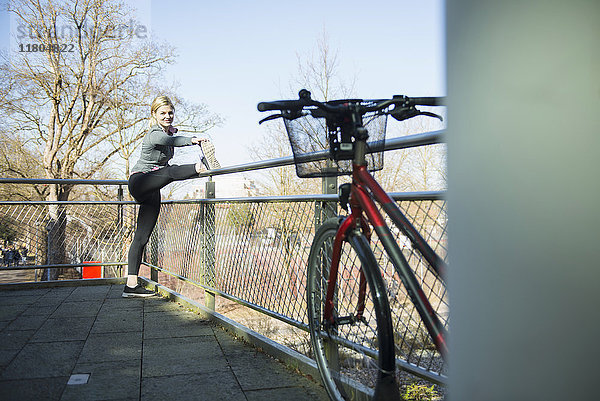 Frau in Sportkleidung beim Stretching auf einer Brücke mit Fahrrad im Vordergrund