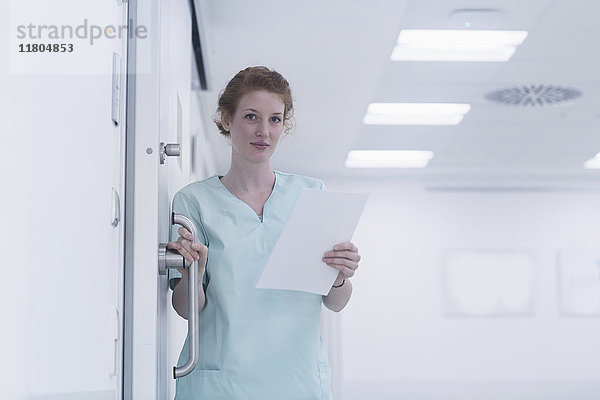 Porträt einer Krankenschwester  die eine Türklinke und Krankenblätter hält