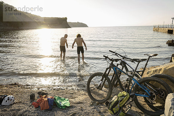 Männer in Radlerhosen stehen im Wasser am Strand