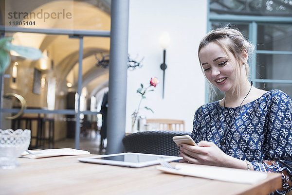 Lächelnde junge Frau  die in einem Restaurant sitzt und mit ihrem Handy Nachrichten schreibt