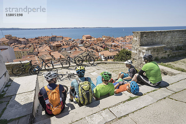 Radfahrer  die auf einer Treppe sitzen und eine verstopfte Stadt am Meer betrachten