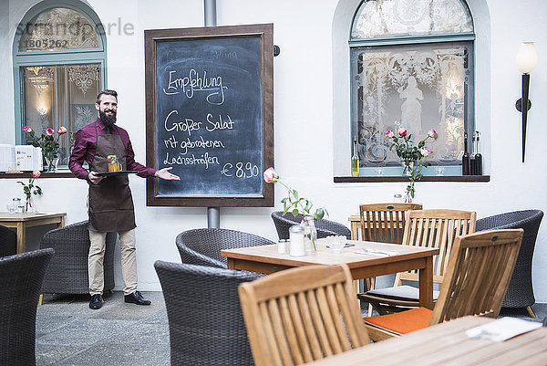 Junger Mann zeigt auf die Speisekarte eines Restaurants mit Kreide