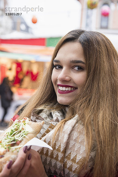 Porträt einer jungen Frau beim Essen auf dem Weihnachtsmarkt