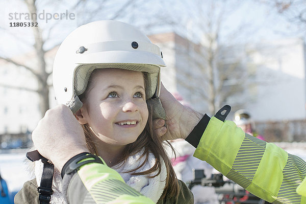 Mädchen wird von Mann beim Tragen eines Helms unterstützt