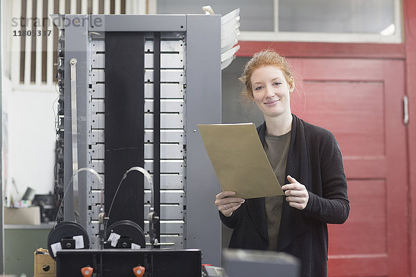 Porträt einer lächelnden Frau  die an einer Druckmaschine steht und ein Dokument hält