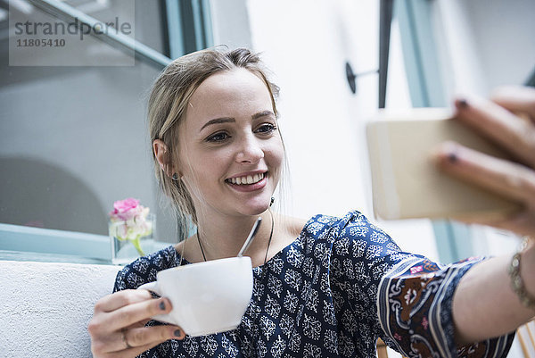 Junge Frau hält Kaffeetasse und nimmt Selbstporträt im Restaurant