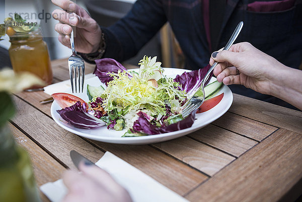 Ausgeschnittenes Bild von zwei Menschen  die eine Gabel halten und Salat essen