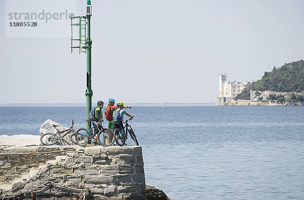 Mountainbiker  die am Meer stehend auf die Aussicht zeigen