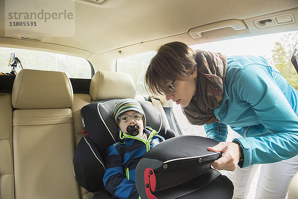 Mutter  die ihren Sohn mit Schnuller im Mund im Kindersitz im Auto anschnallt