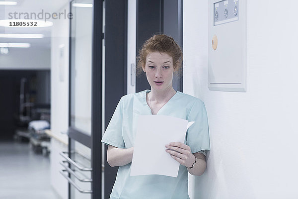 Schockierte Krankenschwester liest Krankenblatt und lehnt sich an die Wand