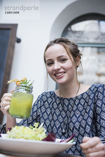 Porträt einer jungen Frau  die einen Mocktail in einem Glas neben einer Salatschüssel hält