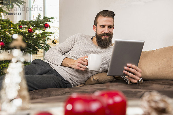 Mann benutzt digitales Tablet und trinkt zu Hause Kaffee