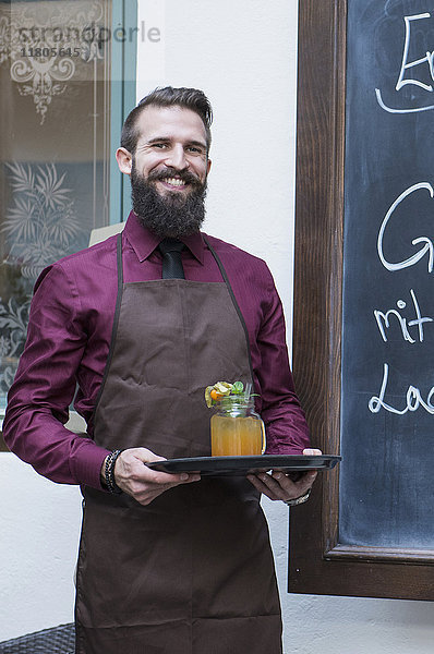 Lächelnder junger Mann mit Mocktail auf einem Tablett