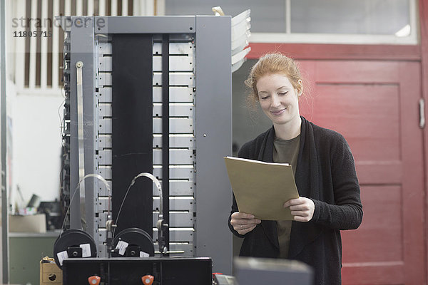 Lächelnde Frau steht an einer Druckmaschine und hält ein Dokument