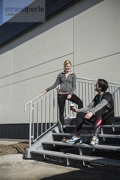 Mann und Frau in Sportkleidung entspannen sich nach dem Training auf einer Treppe
