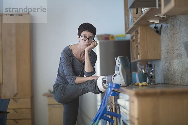 Porträt einer Frau  die ihr gebrochenes Bein auf der Küchenarbeitsplatte ausruht