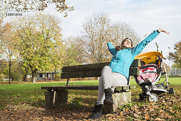 Mutter streckt sich auf einer Parkbank mit Kinderwagen