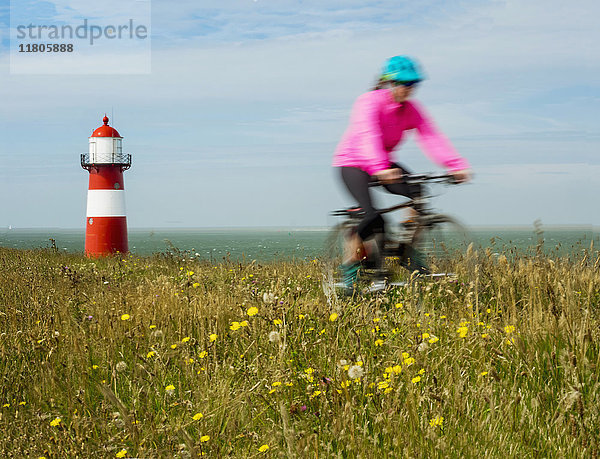 Frau fährt Fahrrad auf einem Feld in der Nähe des Leuchtturms