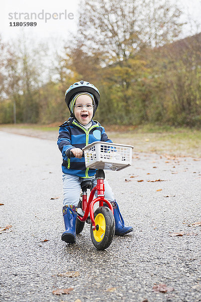 Kleiner Junge fährt lachend mit seinem Laufrad auf einer Straße
