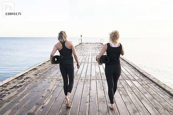 Zwei Frauen tragen Turnmatten und gehen auf dem Pier spazieren