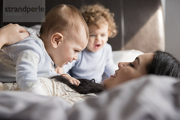 Kaukasische Mutter liegt auf dem Bett und spielt mit ihren Söhnen