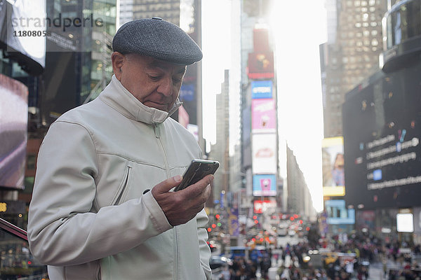 Hispanischer Mann  der in einer überfüllten Stadt eine SMS auf seinem Handy schreibt