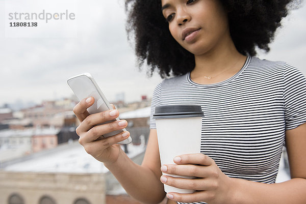 Afroamerikanische Frau trinkt Kaffee und schreibt eine SMS mit dem Handy