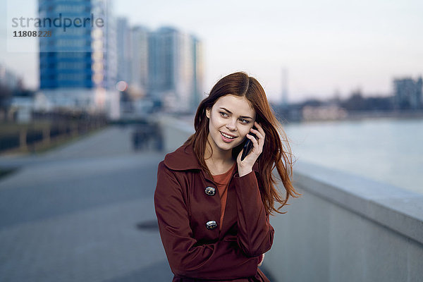Kaukasische Frau  die am Wasser mit einem Handy telefoniert