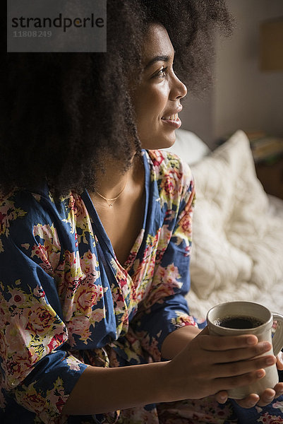 Afroamerikanische Frau sitzt im Bett und trinkt Kaffee