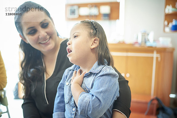 Hispanische Mutter beobachtet Tochter mit Down-Syndrom  die auf den Hals zeigt