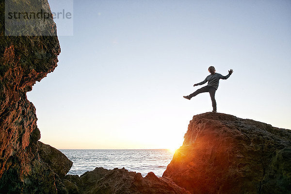 Kaukasischer Mann balanciert auf einem Felsen am Meer