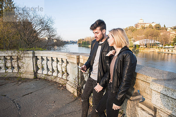 Kaukasisches Paar  das in der Nähe eines Flusses mit dem Handy telefoniert