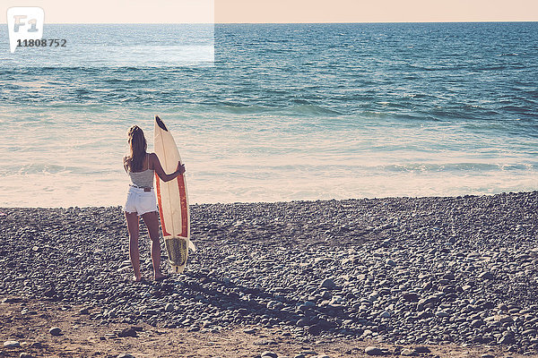 Kaukasische Frau steht am Strand und hält ein Surfbrett