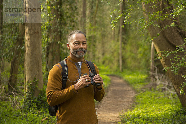 Afroamerikanischer Mann steht auf einem Pfad im Wald und hält ein Fernglas