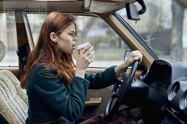 Wütende kaukasische Frau fährt Auto und trinkt Kaffee