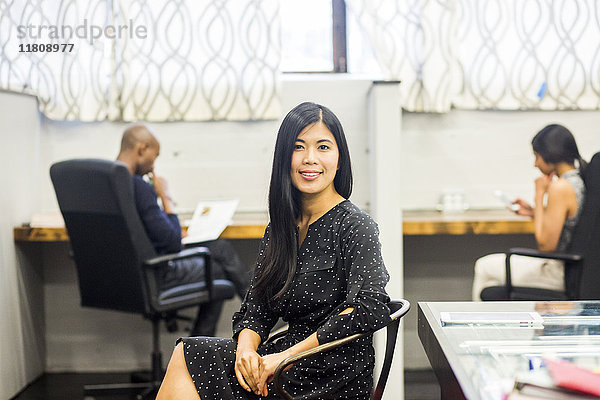 Porträt einer lächelnden asiatischen Frau  die im Büro sitzt
