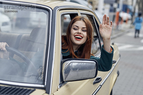 Lächelnde kaukasische Frau fährt Auto und winkt