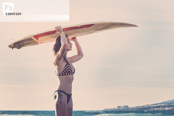 Kaukasische Frau steht am Strand und hält ein Surfbrett