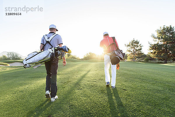 Männer tragen Golftaschen auf einem sonnigen Golfplatz