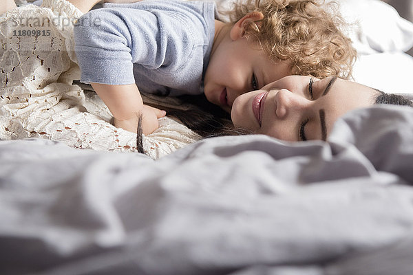 Kaukasische Mutter auf dem Bett liegend und ihren Sohn umarmend