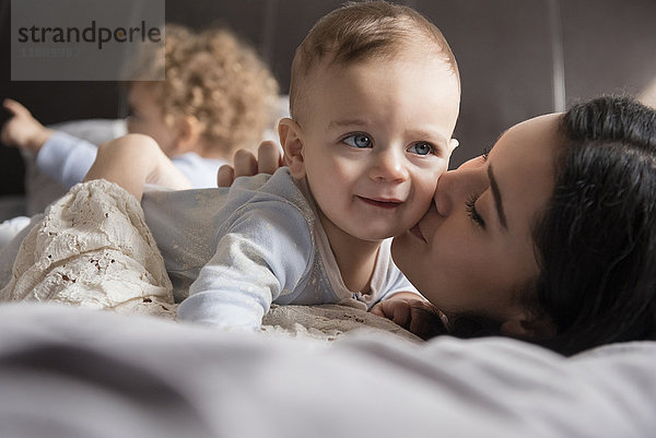 Kaukasische Mutter liegt auf dem Bett und küsst ihren kleinen Sohn