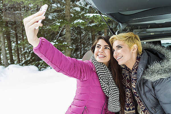 Frauen am Auto posieren für Handy-Selfie im Winter