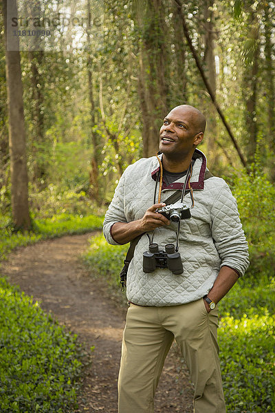 Afroamerikanischer Mann steht auf einem Pfad im Wald und hält eine Kamera